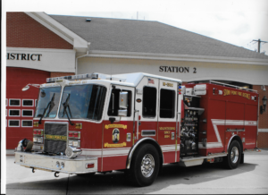 A red and white fire truck labeled "STONY POINT FIRE DISTRICT" is parked outside a fire station with "STATION 2" and red garage doors visible in the background.