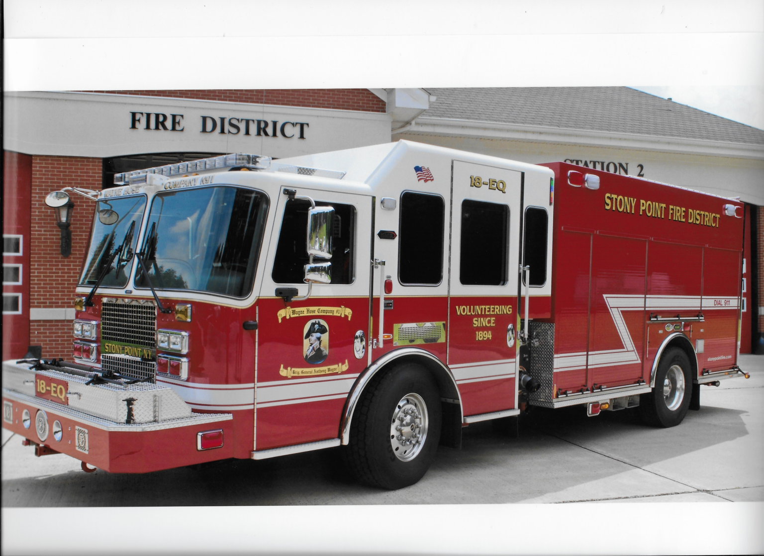 A red fire truck labeled "Stony Point Fire District" is parked in front of a fire station with a "Station 2" sign. The truck has white detailing and various fire department insignias on the side.